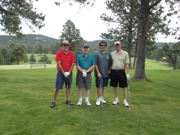 A foursome poses under the pines at the Andy Smith Sr. INSPIRE Golf Tournament